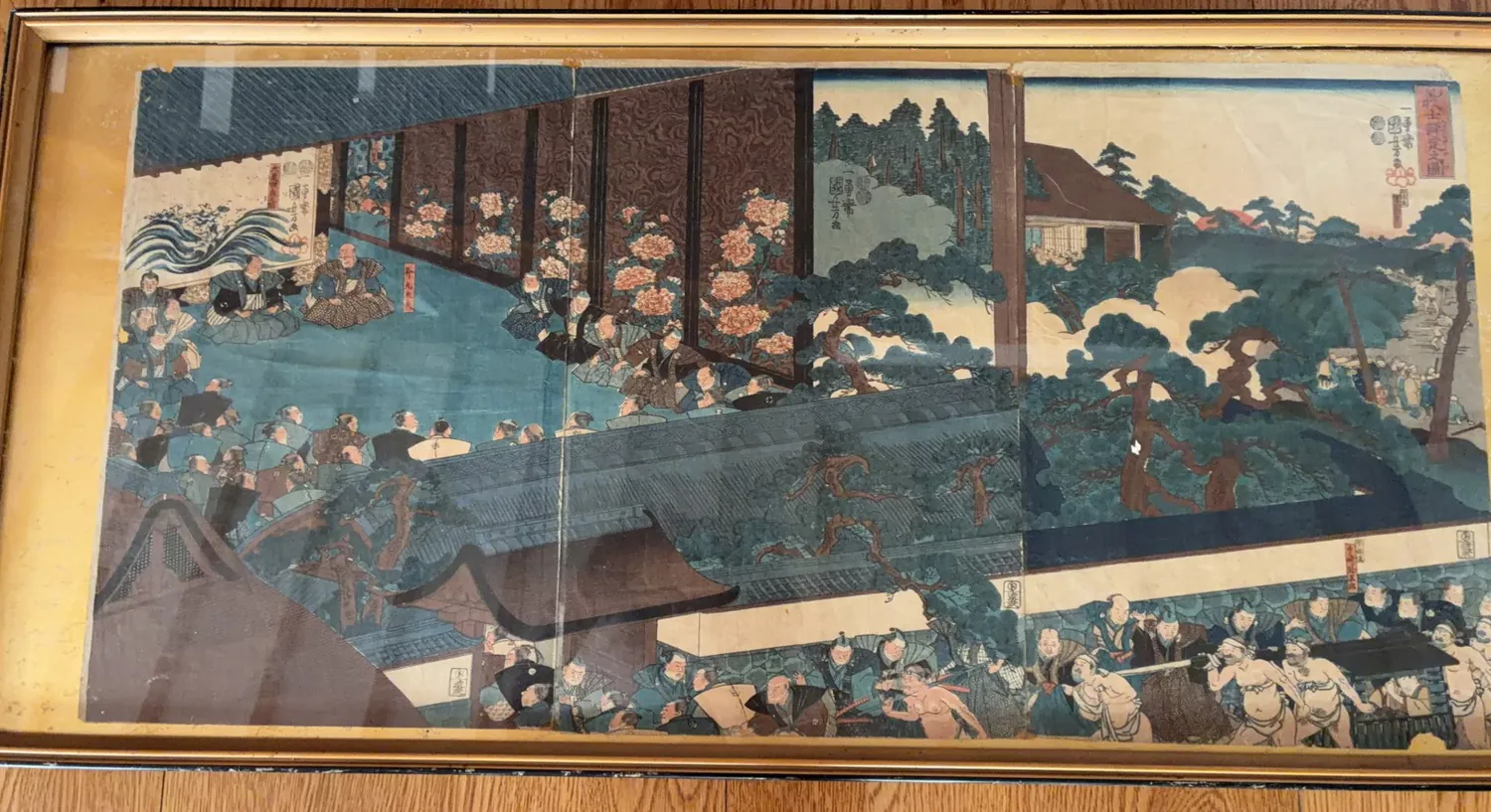 額装された浮世絵 三枚続の実物写真。御殿と庭園を背景に、多くの武士や相撲を取る人物が細密に描かれている。
